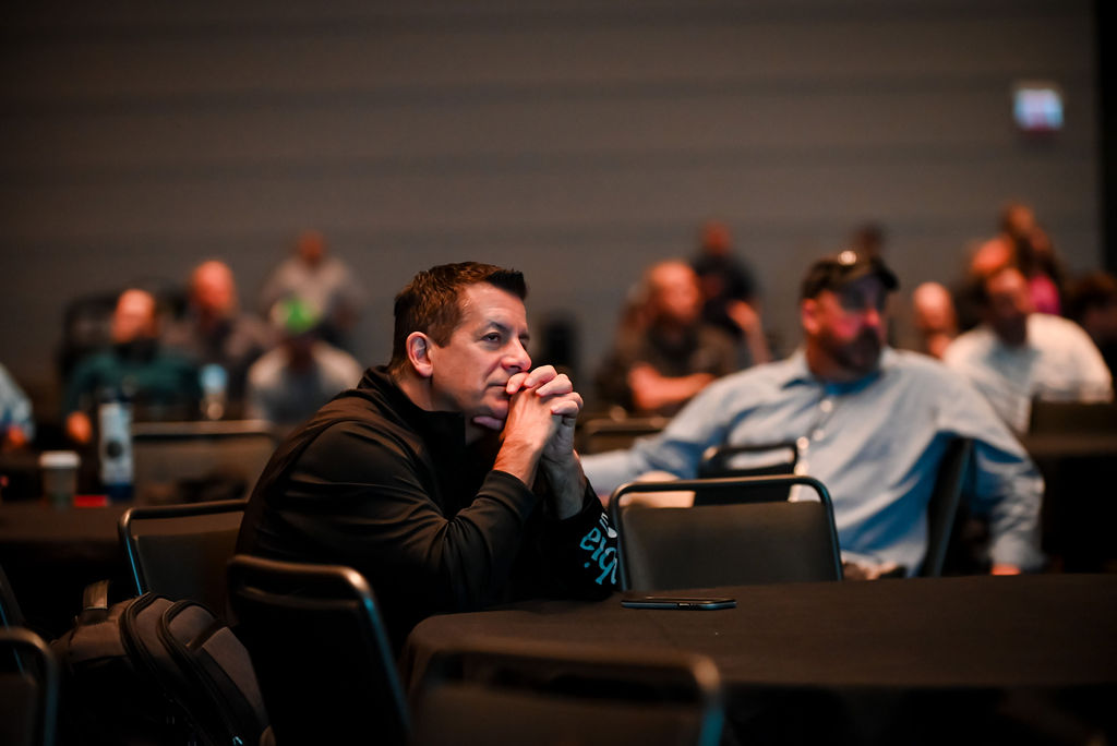 An attendee sits at a table listening attentively during a conference session.