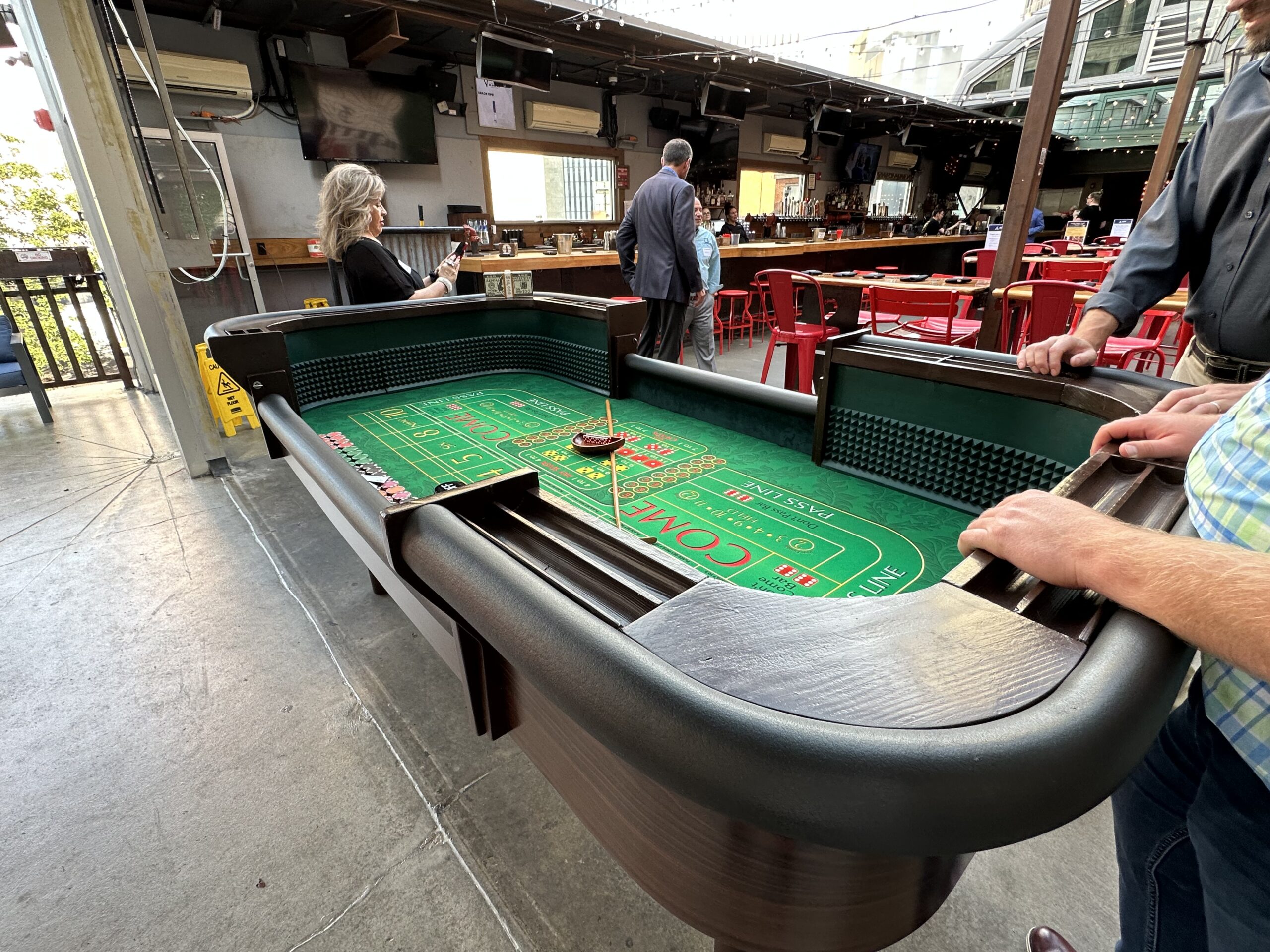 Craps table set up inside a bar-style event space as attendees gather nearby.