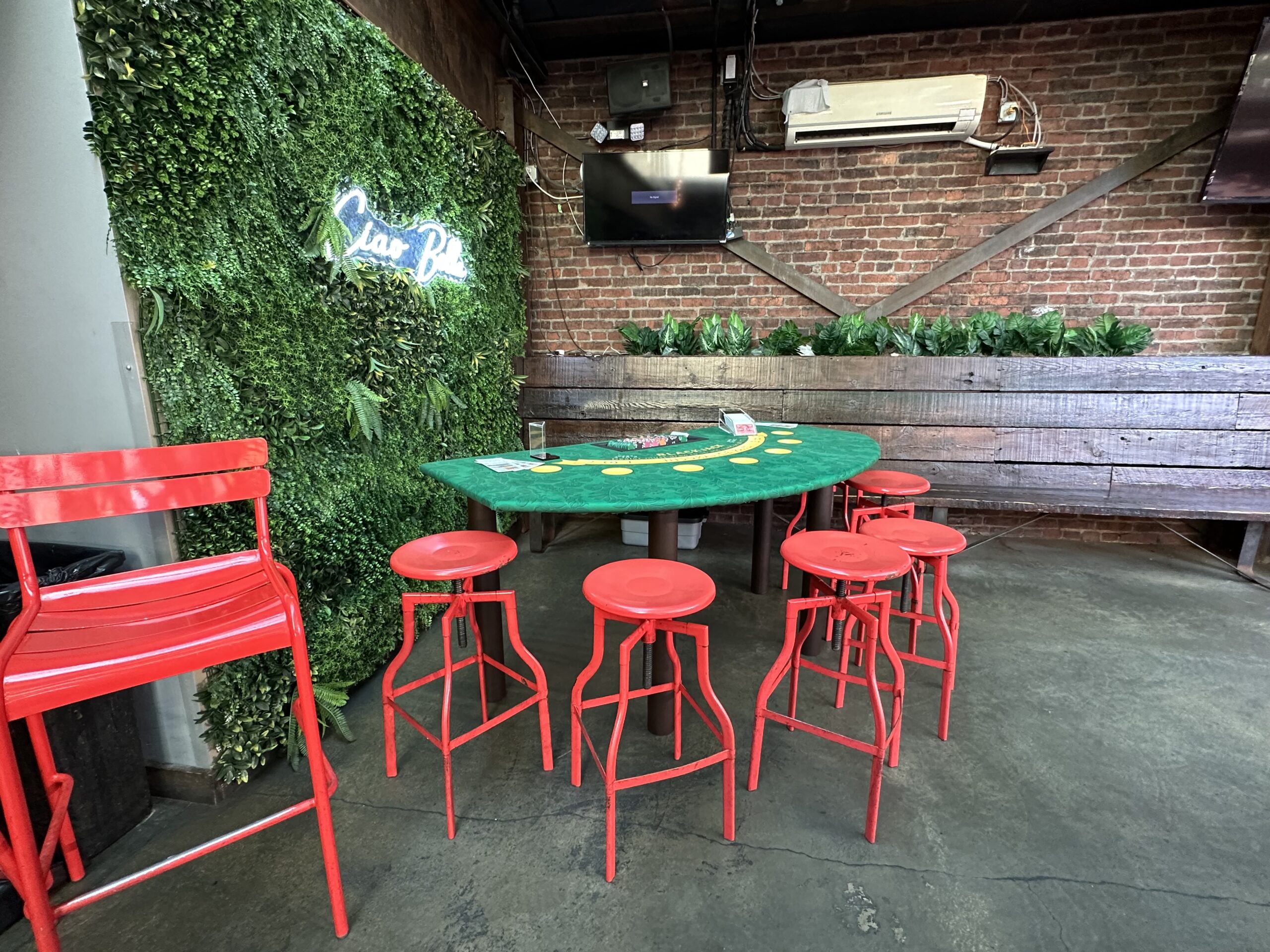 Green felt casino-style table surrounded by red stools inside an indoor bar space.