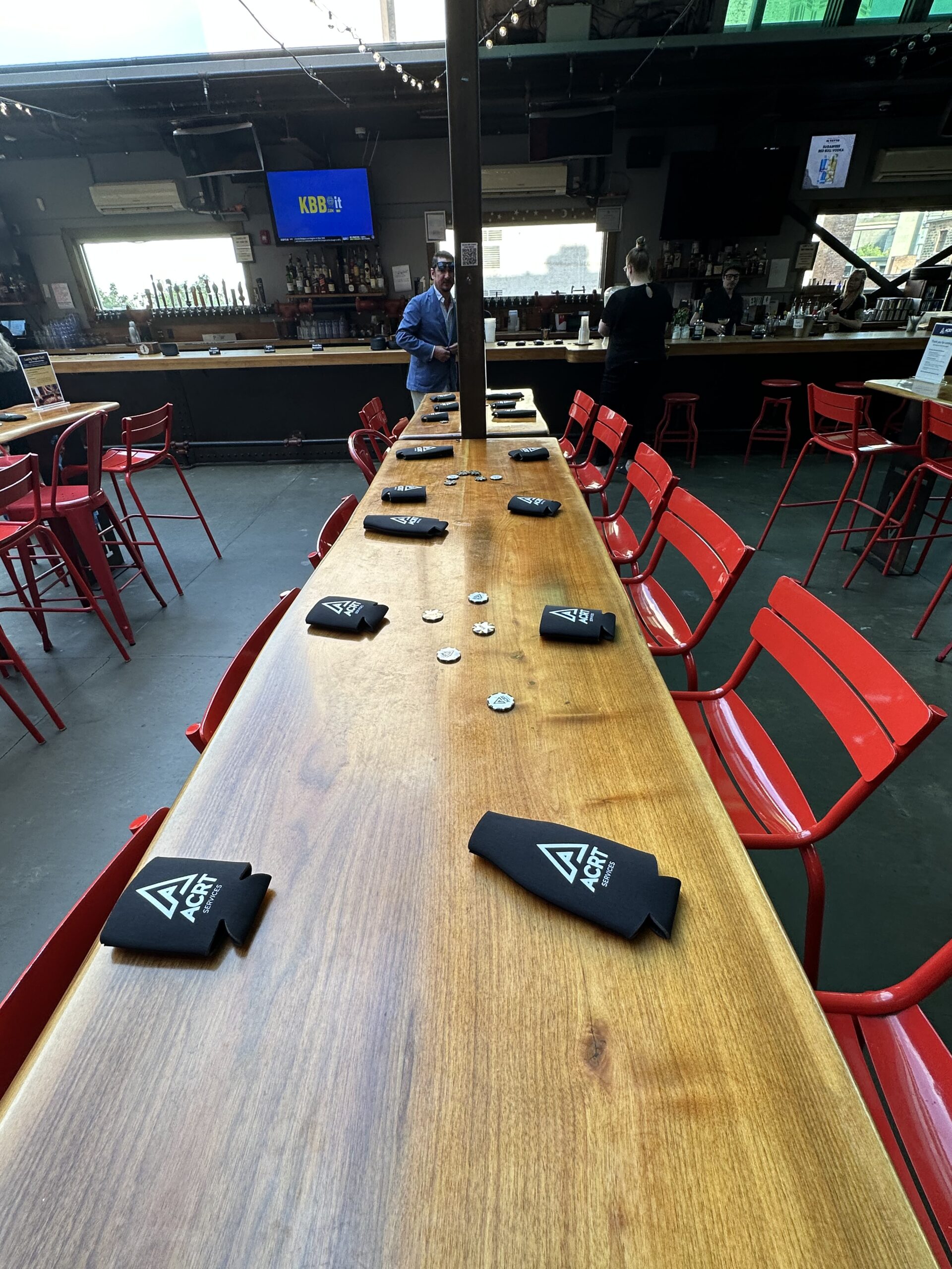 Long wooden table with red chairs set for an event, featuring ACRT-branded drink sleeves.