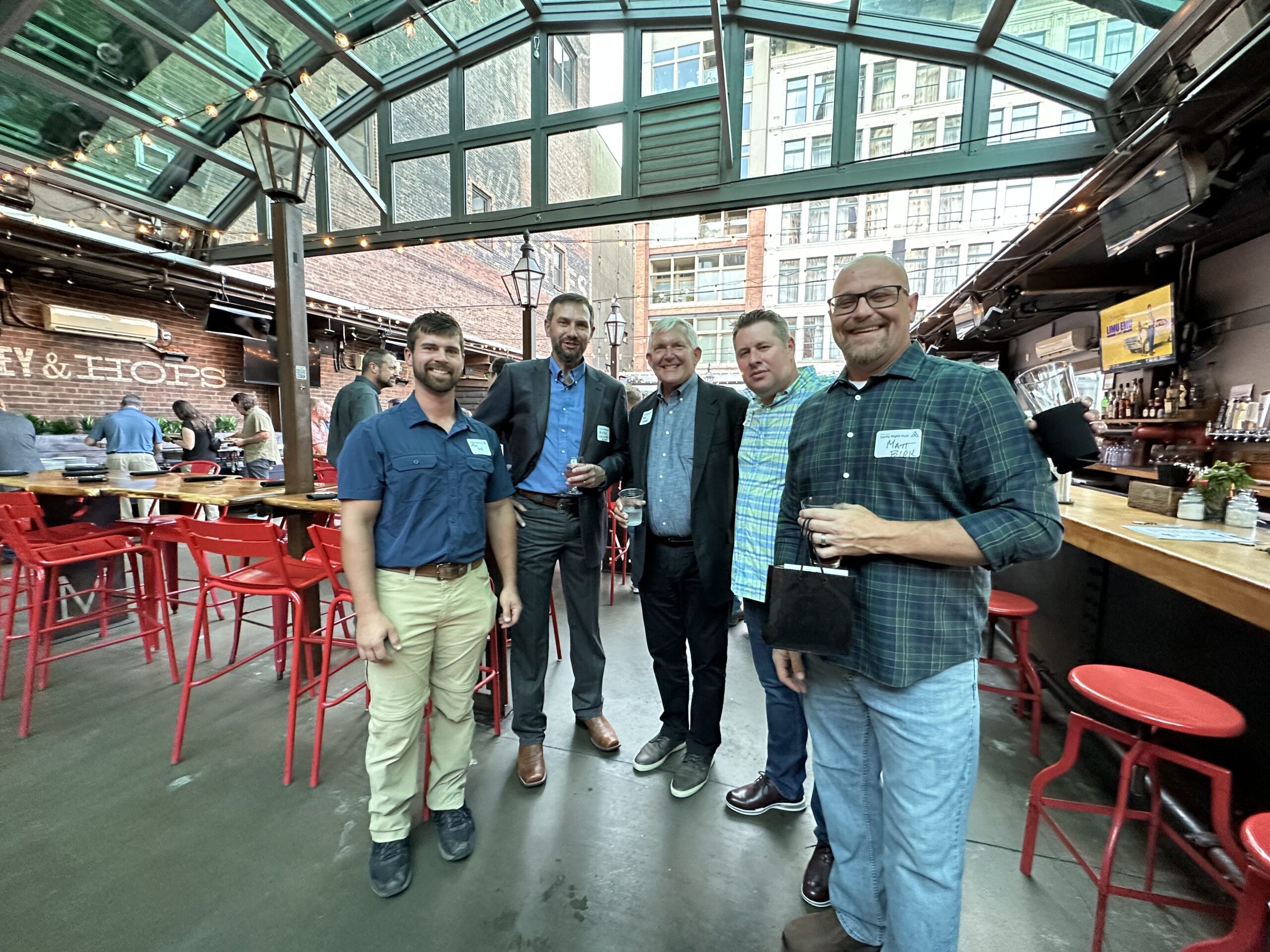 Group of five ACRT employees standing together inside a restaurant or event space, smiling at a team gathering.