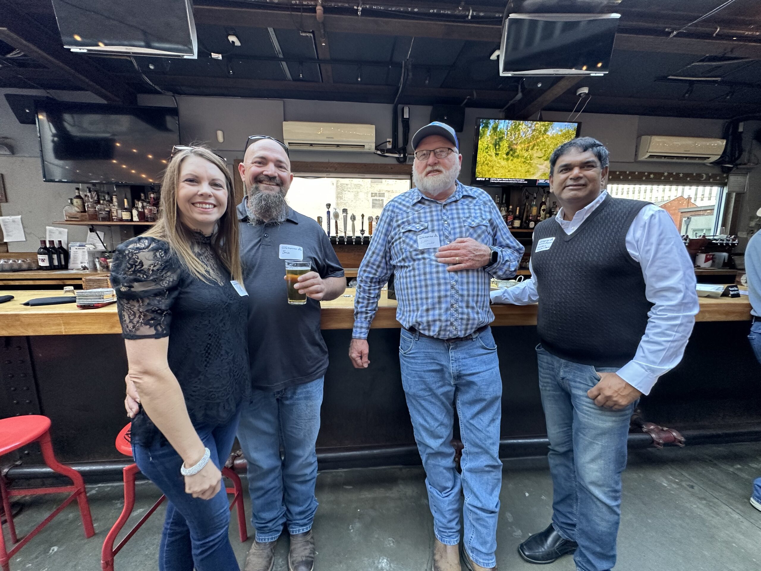 Four attendees stand smiling together at a bar during a networking event.