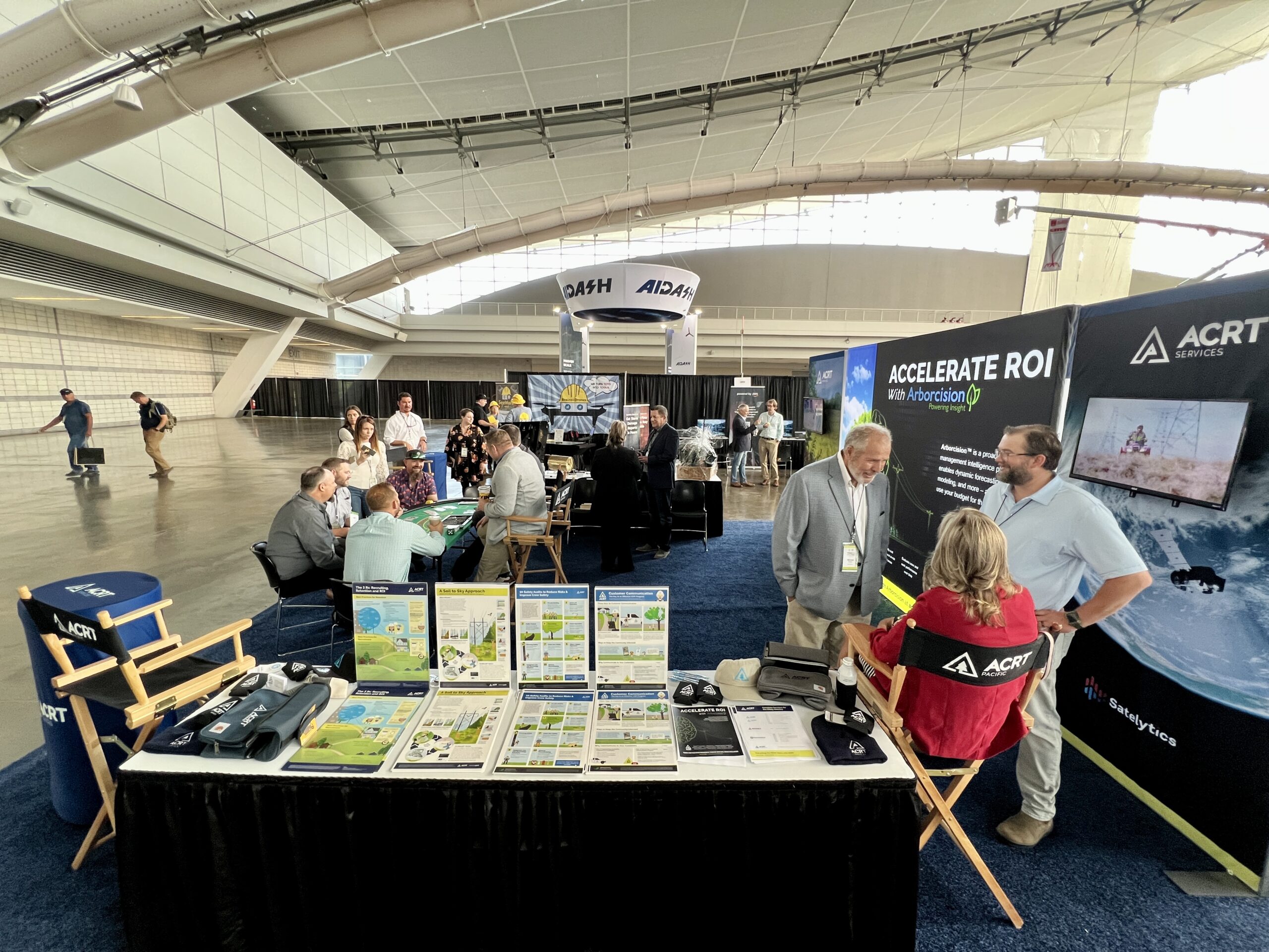 ACRT Services trade show booth with attendees networking and viewing displays in a large convention hall.