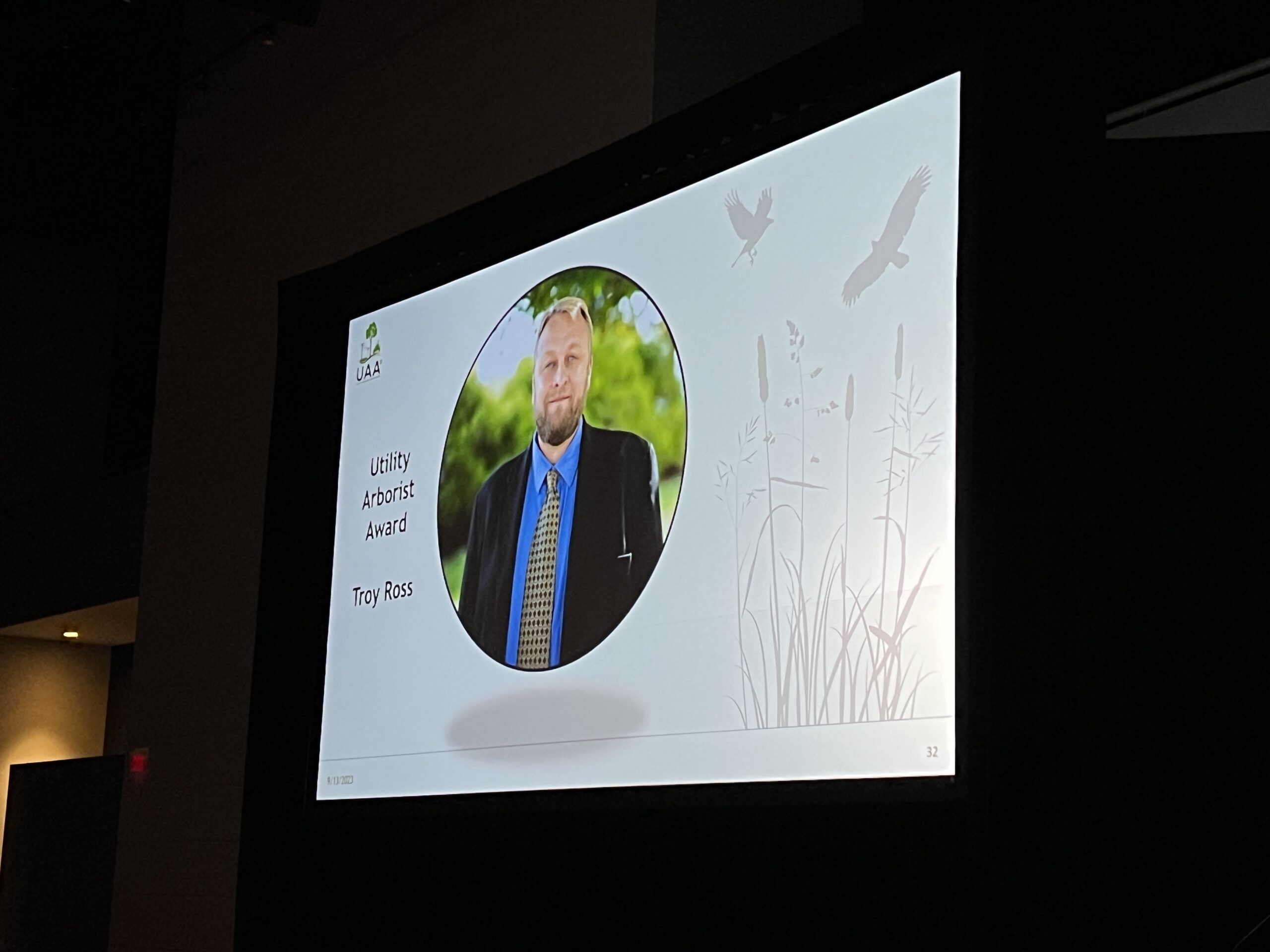 A projected conference slide displays a portrait of Troy Ross labeled “Utility Arborist Award.”