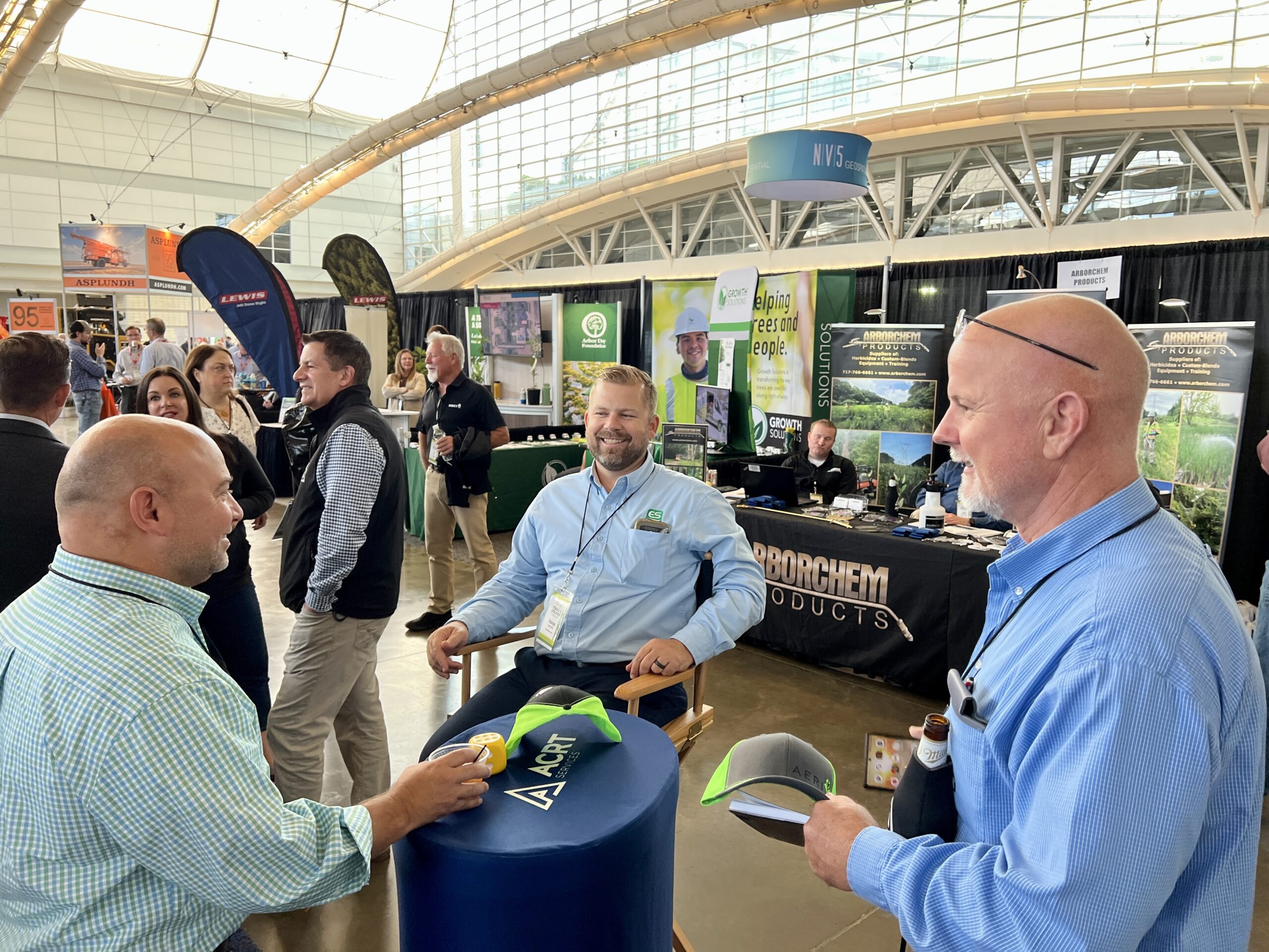 Attendees chat and network around an ACRT-branded table at a trade show floor.